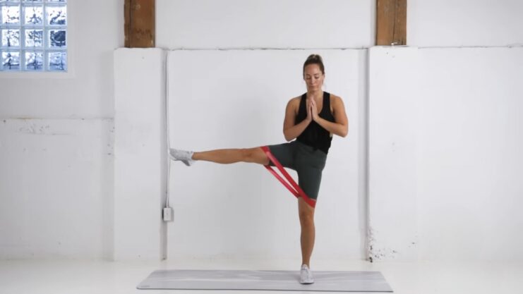 A Woman Performing a Resistance Band Workout, Balancing on One Leg While Extending the Other Leg Sideways for Strength and Flexibility Training