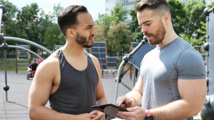 Two Fitness Trainers Having a Discussion Outdoors While Reviewing Information on A Tablet