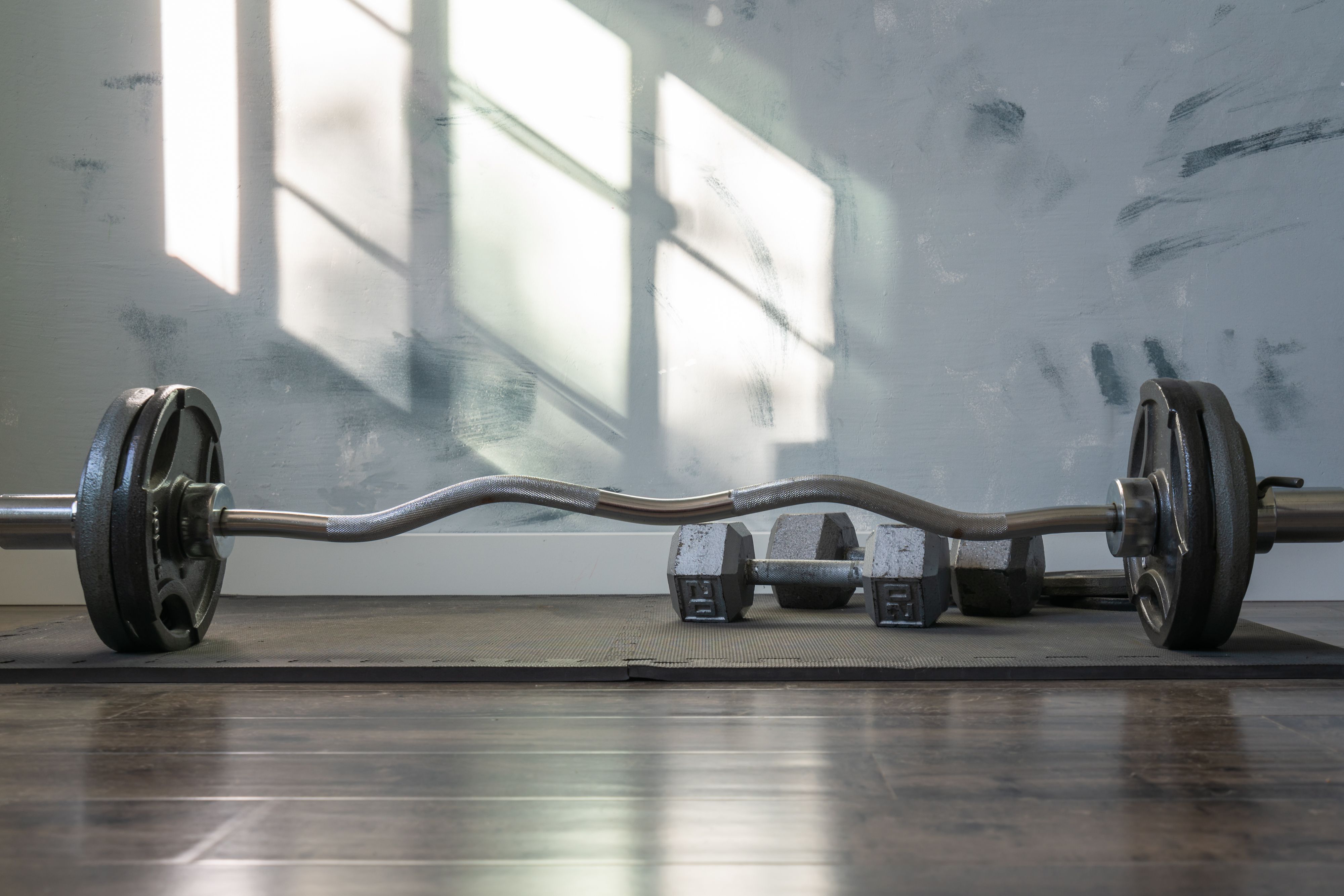 Barbell and dumbbells on a gym mat with sunlight streaming through the window